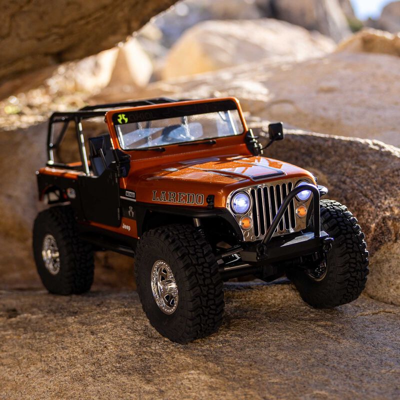 Axial SCX10 III Jeep CJ-7 Copper Laredo crawling over rocks outdoors with headlights on